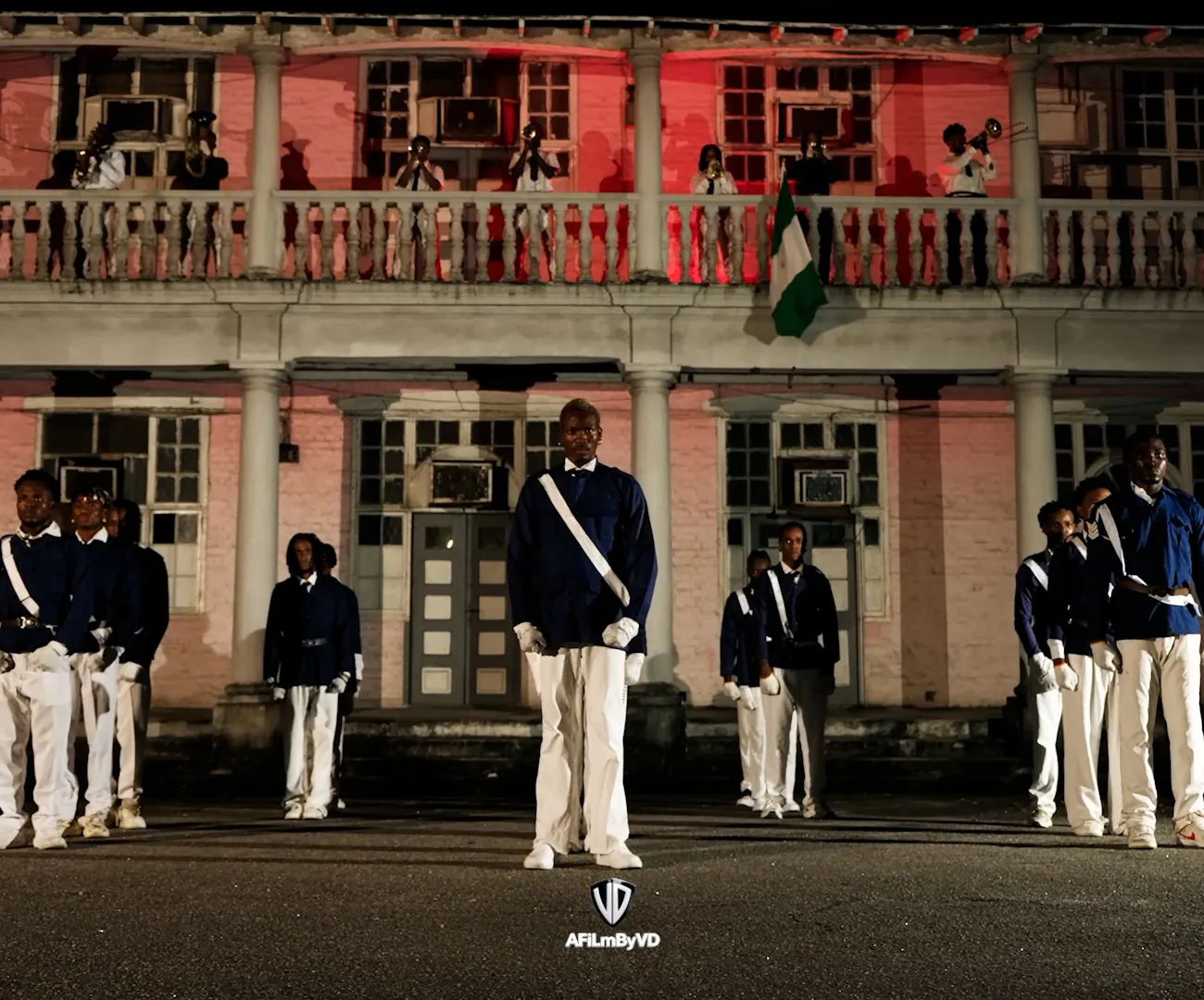 Uniformed performers standing in formation before a colonial-era building at night.